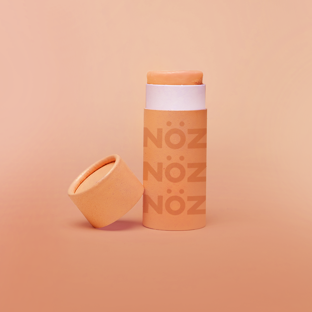 Noz Sunscreen in orange, with the cap off showing the stick of colorful sunscreen inside