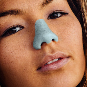 A woman's face close up wearing Noz biodegradable sunscreen on her nose in blue.